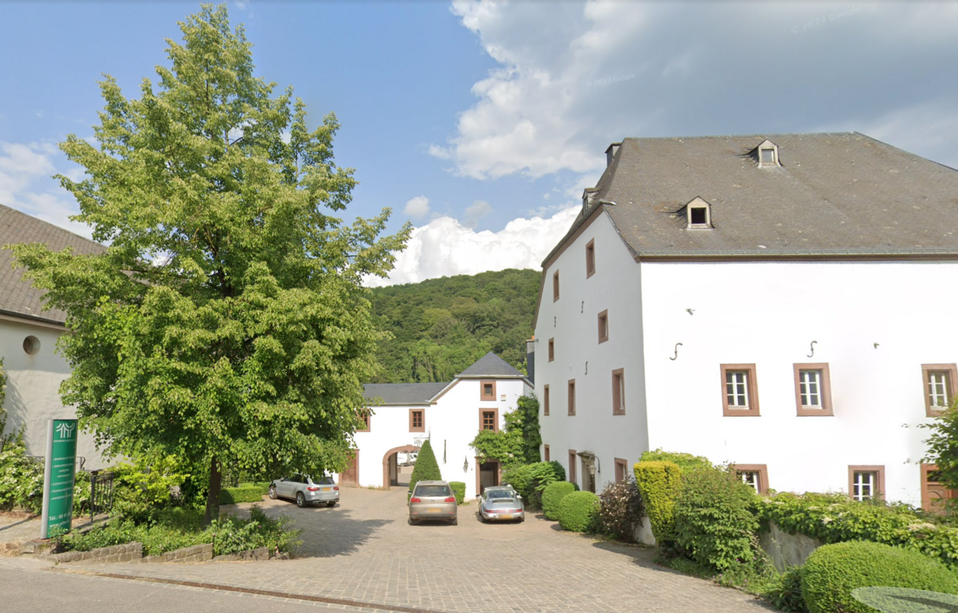 Courtyard of white historic buildings with parked cars under a large tree